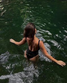 a woman in a black bathing suit wading in the water with her arms outstretched