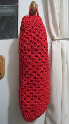 a red crocheted bag hanging on the wall next to a window with curtains