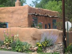 an adobe style house with flowers and plants around it on the side of the road