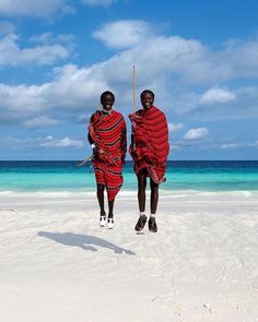 two men in red and black robes walking on the beach