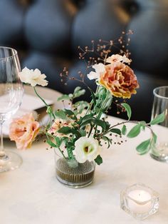 flowers in a vase on a table with wine glasses and silverware, along with candles