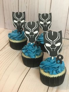 cupcakes with blue frosting and black masks on them sitting on a table