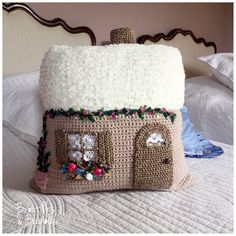 a crocheted house pillow sitting on top of a bed