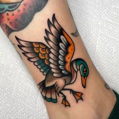 a bird tattoo on the foot of a person's leg, with an orange and blue bird in the background