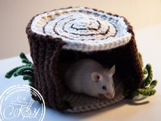 a white rat sitting in a crocheted house made to look like a tree stump