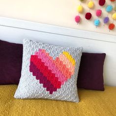 a crocheted heart pillow sitting on top of a bed next to a wall