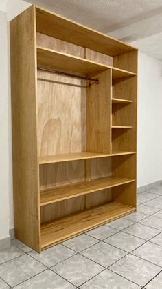 an empty wooden bookcase sitting on top of a white tiled floor next to a wall