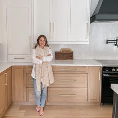 a woman standing in a kitchen next to an oven and counter top with her arms crossed