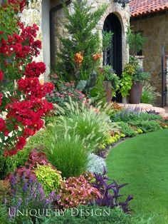 a garden with lots of flowers and plants in the front yard, next to a stone building