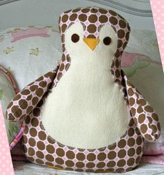 a stuffed penguin sitting on top of a bed next to a pink and white polka dot pillow