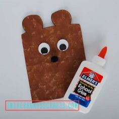 a paper bag with a bear face next to a bottle of glue and an eraser