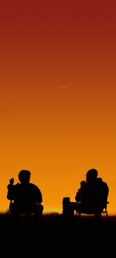 two people sitting in chairs watching the sun set with an airplane flying over their heads