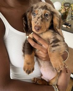 a woman holding a brown and black puppy in her arms while wearing a white tank top