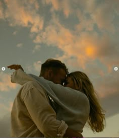 a man and woman are kissing in front of the sky at sunset with clouds behind them