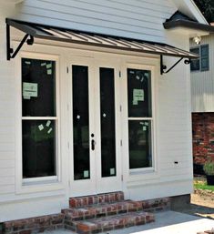 a white house with black awnings and brick steps