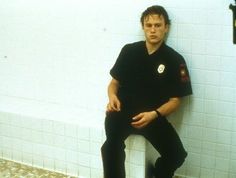 a man sitting on top of a white toilet in a bathroom next to a tiled wall