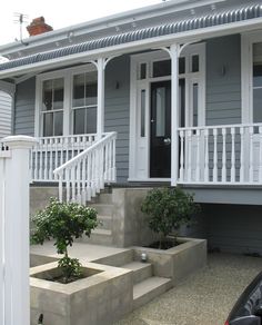 a grey house with white railings and steps leading up to the front door area