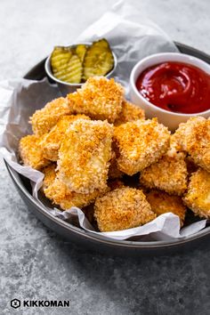 some fried food is in a bowl with ketchup and pickles on the side