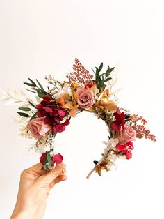 a hand holding up a flower crown made out of flowers and greenery on a white background