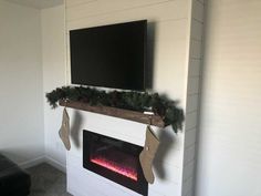 a flat screen tv mounted above a fireplace with stockings hanging from it's sides