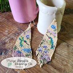 a pair of beaded earrings sitting on top of a table next to a cup