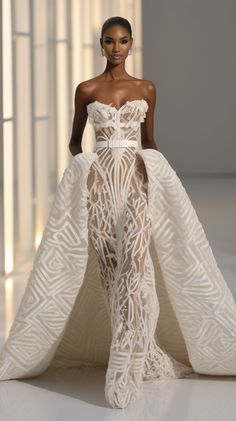 a model in a white gown with an intricate pattern on the skirt and side slit