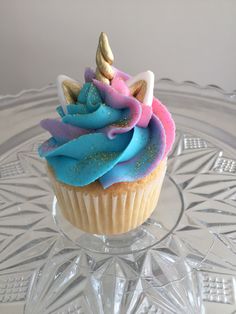 a cupcake with blue, pink and gold frosting on a clear glass plate