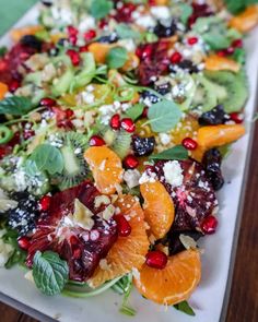 a salad with oranges, avocado, and cranberries on a white plate