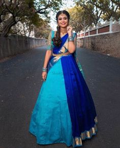 a woman in a blue and gold dress standing on the street with trees behind her