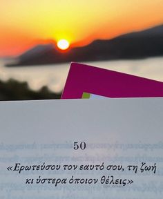 a piece of paper sitting on top of a table next to a book with the sun setting in the background