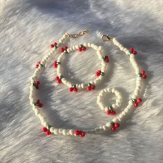 a white beaded necklace with red and green beads is on top of a furry surface