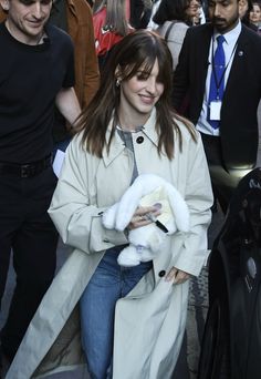 a woman walking down the street carrying a baby in her arms and wearing a trench coat