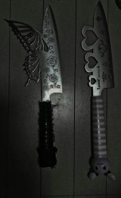 two knives are sitting next to each other on a table in the dark, one is decorated with flowers and hearts