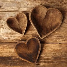 three heart shaped wooden bowls sitting on top of a wooden table