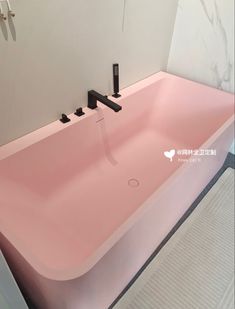 a pink bathtub in a bathroom with black faucets