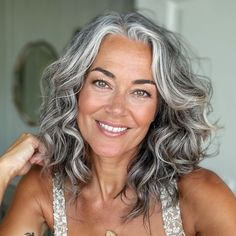 a woman with grey hair is smiling and holding her hand on her shoulder while looking at the camera