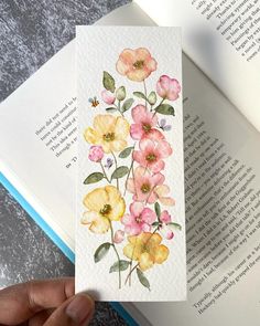 a hand holding an open book with watercolor flowers painted on the front and back