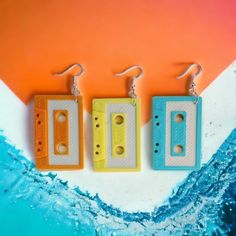 three different colored cassettes are hanging from ear hooks on an orange and blue background