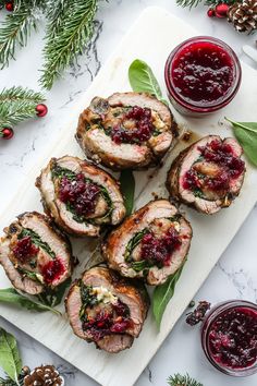 sliced pork with cranberry sauce on a white cutting board surrounded by pine cones and greenery