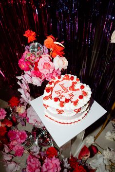 a white cake sitting on top of a table next to pink and red flowers in vases