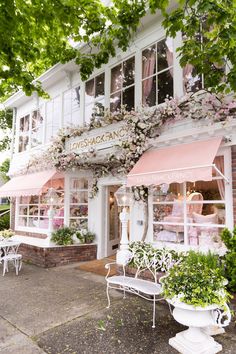 a store front with pink and white awnings on the windows, tables and chairs outside