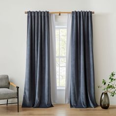 a living room with a chair and window covered in gray drapes, next to a potted plant