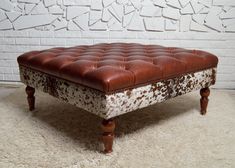 a brown and white leather ottoman sitting on top of a shaggy rug next to a brick wall