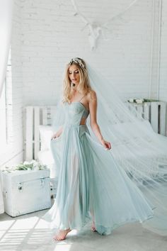 a woman in a blue dress is standing near a white brick wall and wearing a veil