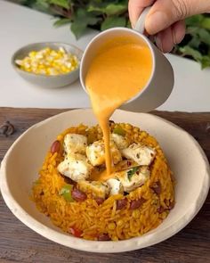 someone is pouring sauce on some food in a white bowl with yellow rice and vegetables