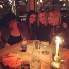 three women are sitting at a table with drinks and candles in front of them, posing for the camera