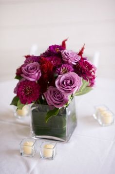 a vase filled with purple flowers sitting on top of a white table covered in candles