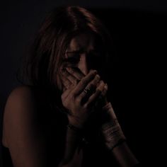 a woman covers her face with her hands while standing in front of a dark background