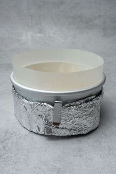 a silver tin container sitting on top of a gray floor next to a white bowl