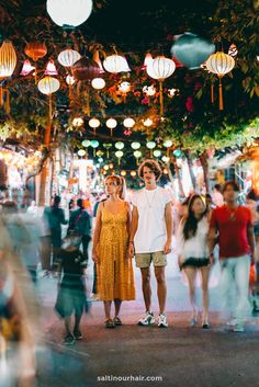 two people standing in the middle of a crowded street with lanterns hanging overhead and onlookers looking at them